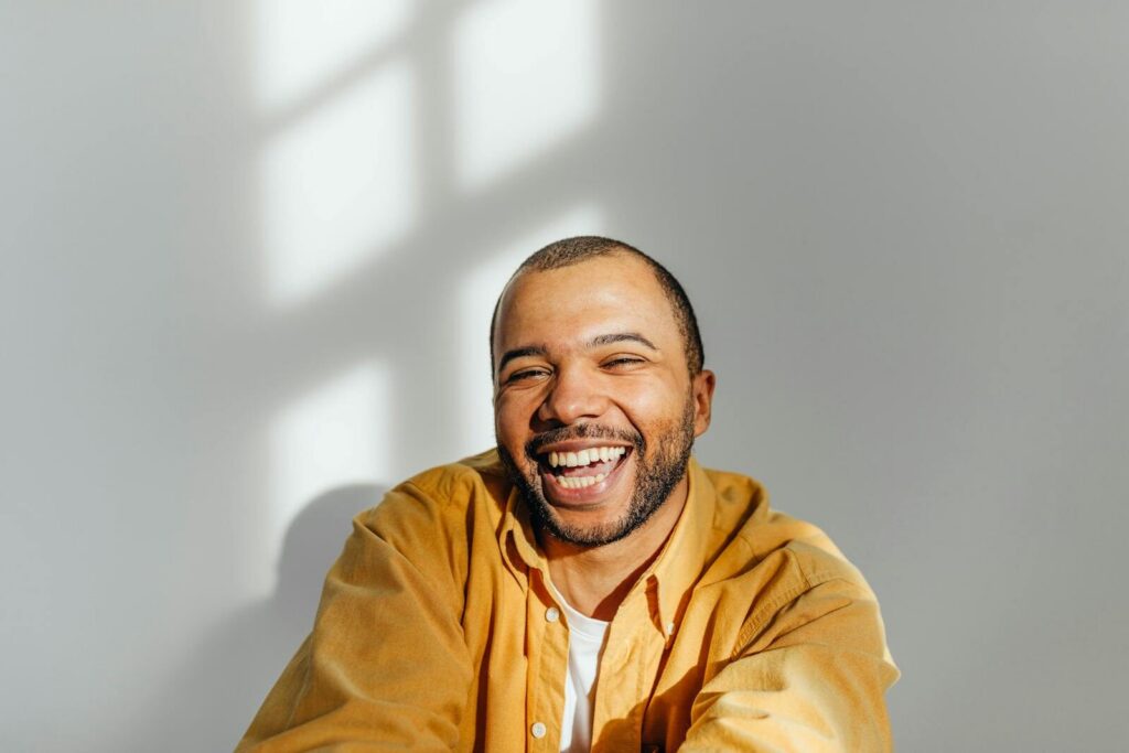 Cheerful man in a yellow shirt laughing in a sunlit room.